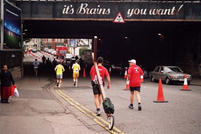 Counties evangelist Clive Cornish runs with his cross during the Cardiff Half Marathon. Running under the bridge advertising says,"It's Brains you want!"